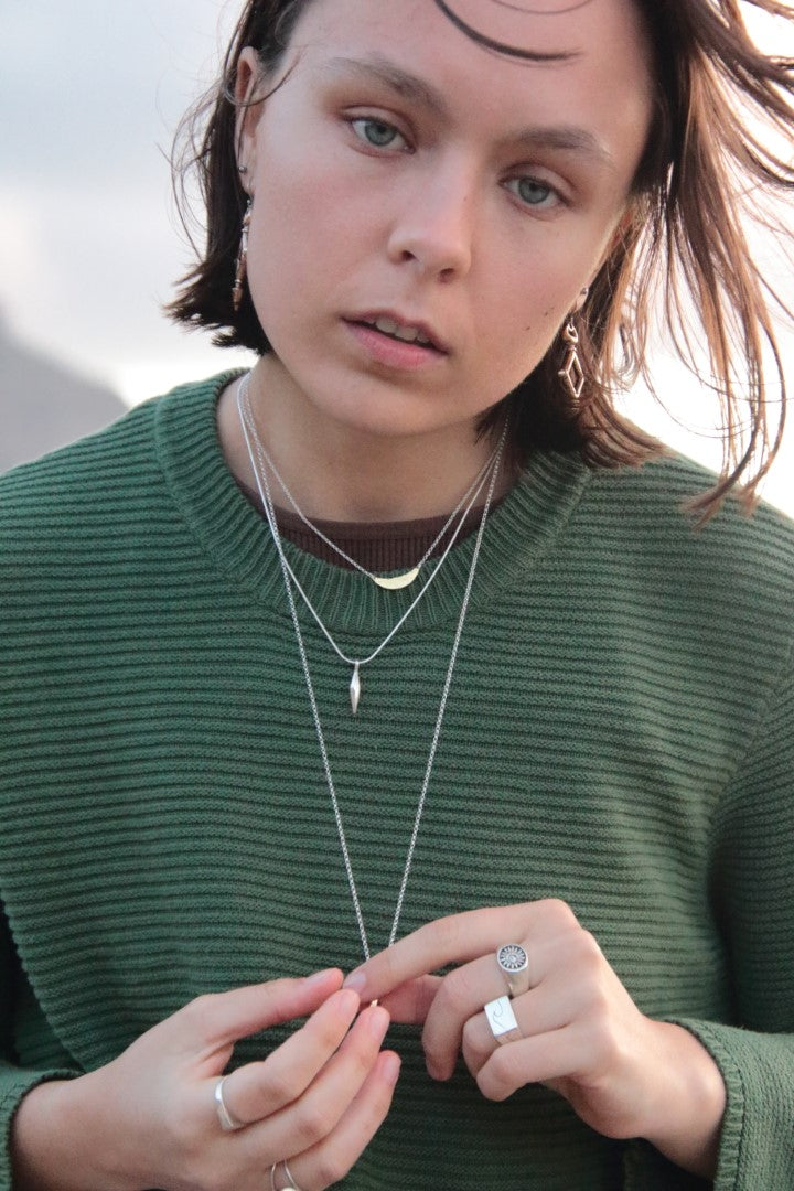 Person wearing a green sweater with layered necklaces and rings.