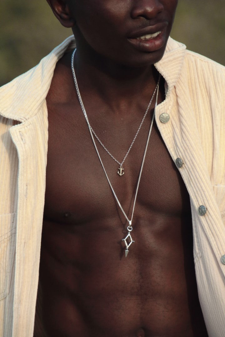 Man wearing a beige shirt with layered necklaces, outdoors.