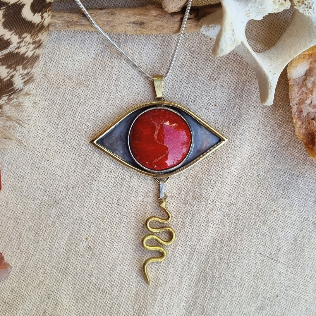 Pendant with coral stone eye design and a snake charm at the bottom on a textured surface