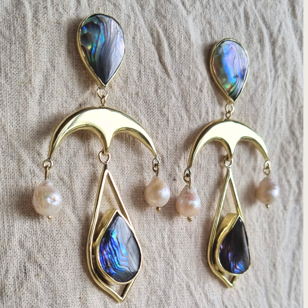 Pair of brass earrings with tear drop abalone shell and pearl drops on a textured fabric background