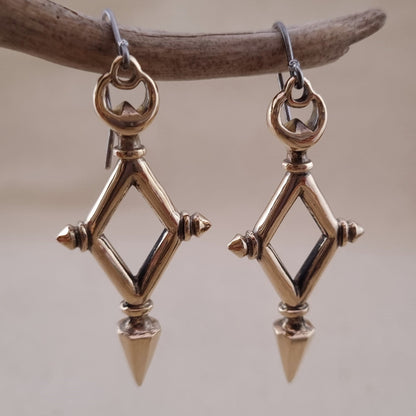 Pair of gold-colored diamond-shaped earrings hanging from a branch.