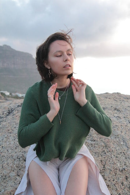 Woman in a green sweater sitting on a rocky surface with mountains in the background