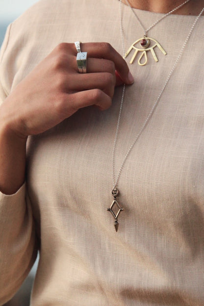 Close-up of a person wearing a gold necklace with a pendant and a ring on a neutral background
