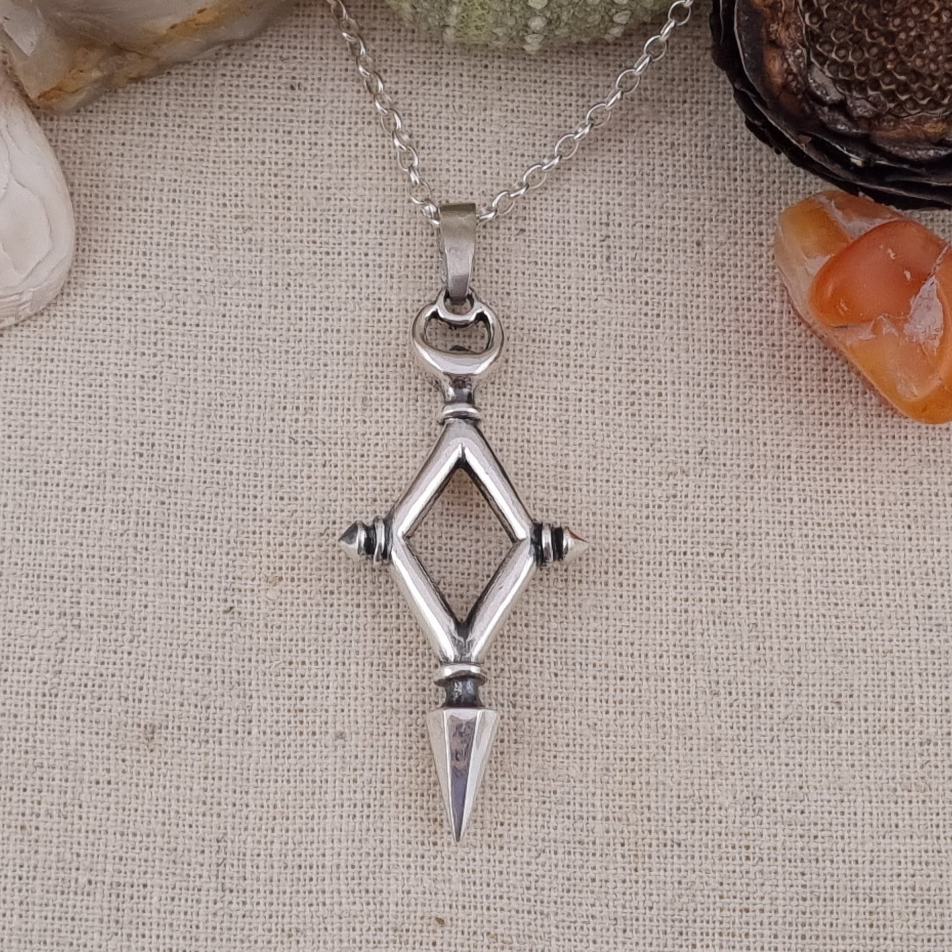 Silver pendant necklace on a textured fabric background with natural elements.