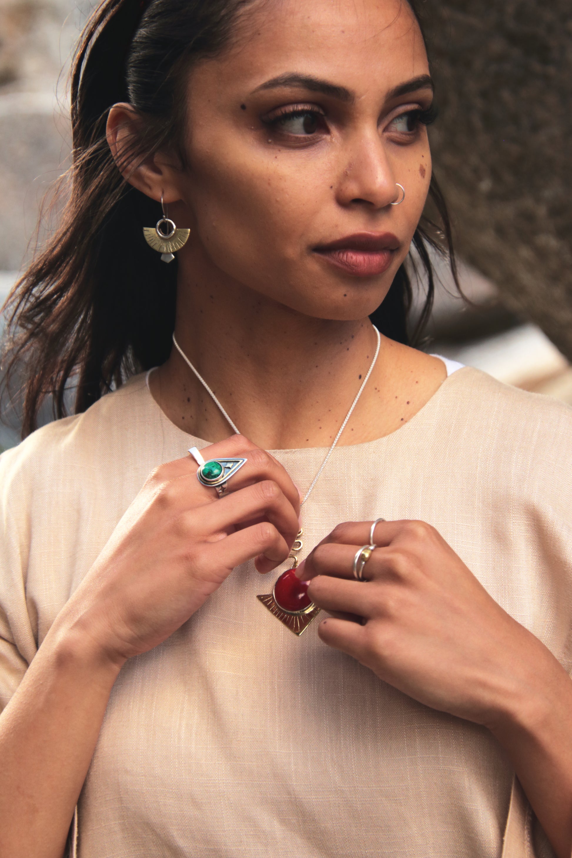 Woman wearing jewelry, including a necklace, ring, and earrings, with a blurred natural background.
