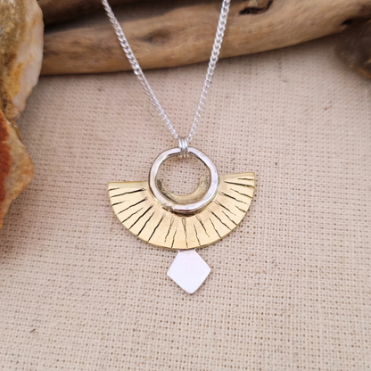 Necklace with a gold and silver pendant on a beige fabric background
