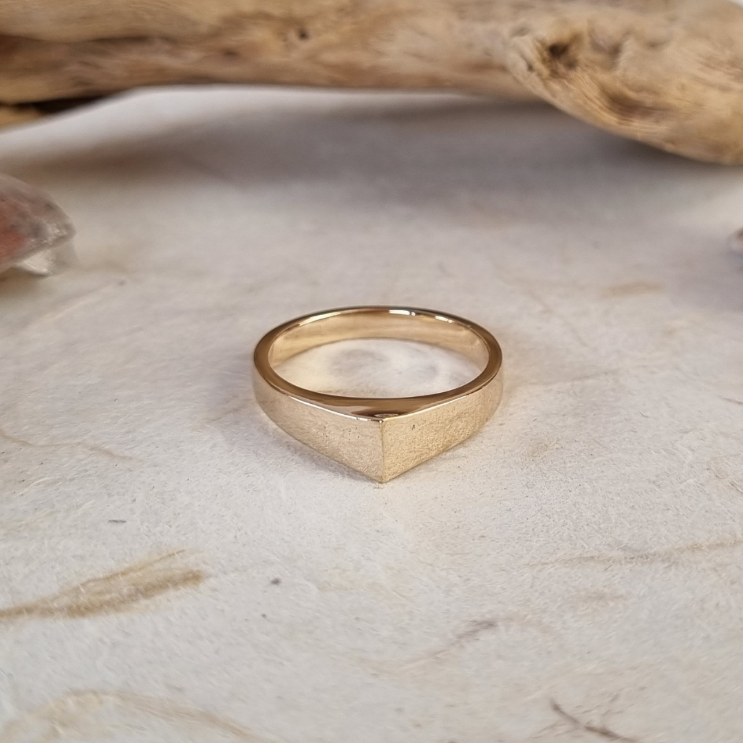 Gold ring on a textured beige surface with a piece of driftwood in the background