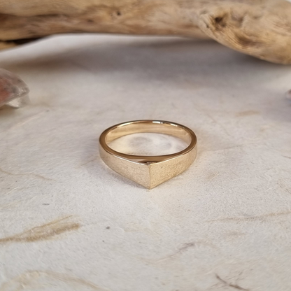 Gold ring on a textured beige surface with a piece of driftwood in the background