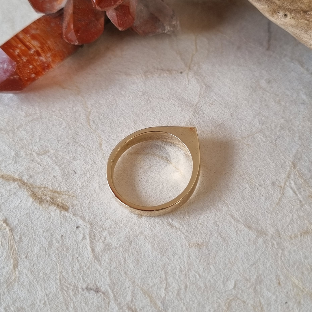 Gold ring with a clear stone on a textured beige surface