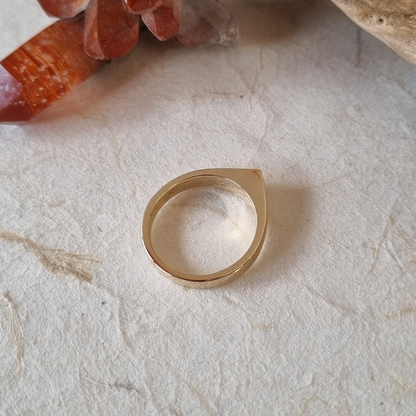 Gold ring with a clear stone on a textured beige surface