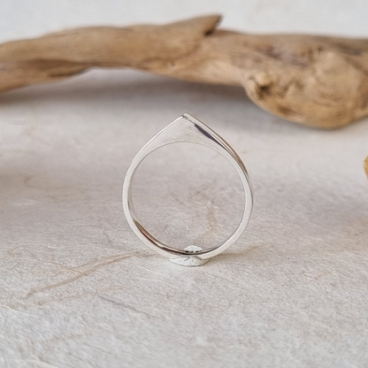 Silver ring on a light stone surface with a piece of driftwood in the background