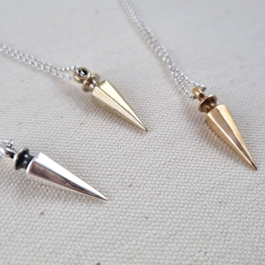 Three spiked Wayfinder Pendants on chains against a light fabric background